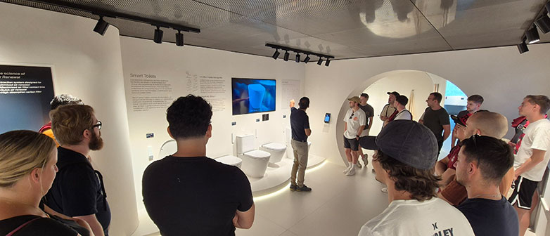 Gruppe bei einer Führung durch eine moderne Ausstellung zu Sanitärtechnik und Toiletten.