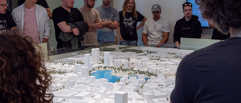 Gruppe Studierender steht um ein Stadtmodell mit einem See in der Mitte