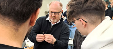 Ein Dozent erklärt zwei Studierenden etwas an einem Gegenstand