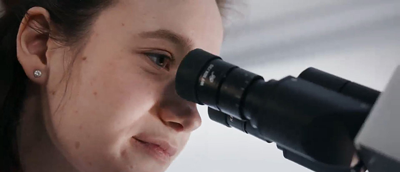 Nahaufnahme einer Frau, die in ein Mikroskop schaut