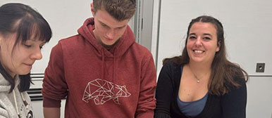 Jill Baumann und zwei Mitstudierende an stehen an einem Tisch