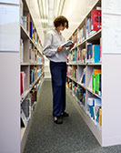 Studierende liest stehend in der Bibliothek zwischen Regalen