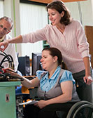 Person im Rollstuhl hört sich in der Werkstatt eine Erklärung der Dozierenden an