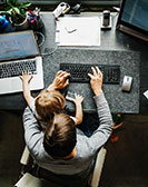 Erwachsene Person bei der Arbeit am Laptop mit Kind auf dem Schoss