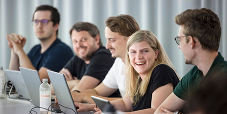 Gruppe von Studierenden mit Laptops an einer Tischreihe