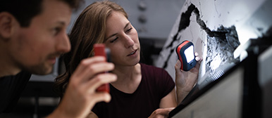 Ein Student und eine Studentin betrachten sich im Dunkeln mit Taschenlampen ein Bauprojekt