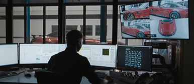 Ein Student sitzt vor mehreren Bildschirmen und der grösste Bildschirm zeigt verschiedene Abbildungen eines roten Autos