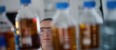 Bild zeigt Studentin aus Profil Medical Engineering mit Schutzbrille vor Regal mit flüssigen Substanzen