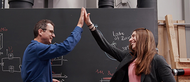 Frau und Mann geben sich ein High-Five vor einer Wandtafel