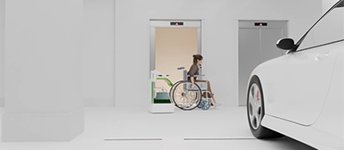 Ein Assistenzroboter begleitet eine Frau im Rollstuhl vom Auto zum Aufzug