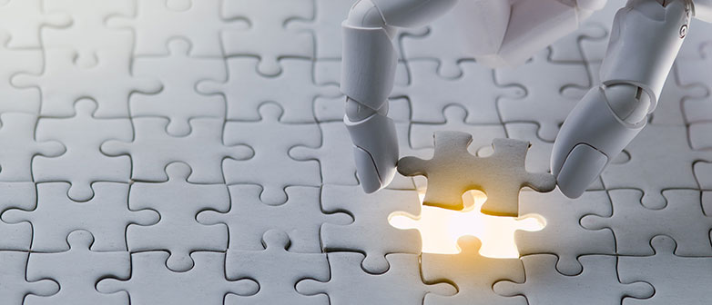 Roboterhand setzt letztes Stück in ein weisses Puzzle.