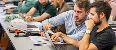 zwei junge maenner am laptop mit bauhelm auf tisch