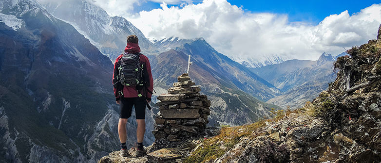 Foto zeigt einen Wanderer, der auf einem Berg den Ausblick über das Alpenpanorama geniesst.