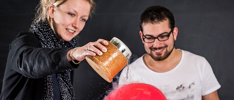 Zwei Studierende leeren eine Flüssigkeit über einen roten Ballon