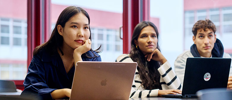 Drei junge Menschen sitzen mit Laptops in einem Klassenraum