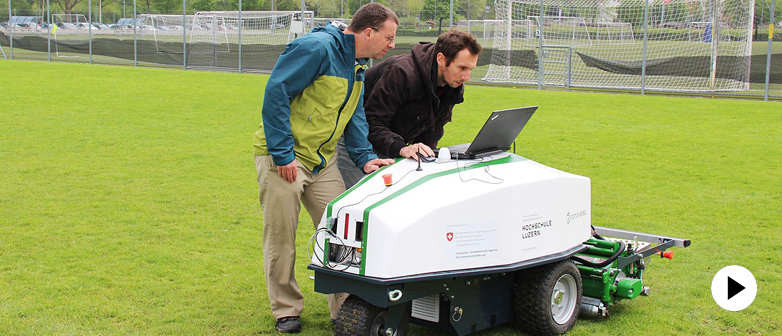 Zwei Experten der Hochschule Luzern programmieren den Mähroboter auf dem Fussballplatz - Link bitte klicken