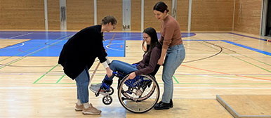 Zwei Frauen helfen einer Frau im Rollstuhl