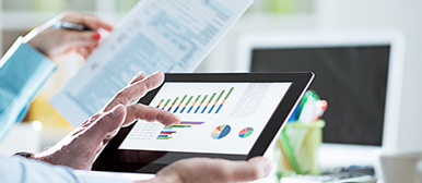 Person analysiert Finanzdaten auf einem Tablet mit Diagrammen und Grafiken, während sie ein Dokument in der Hand hält.