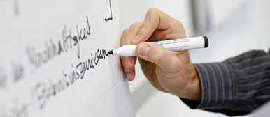 Person die auf ein Whiteboard schreibt