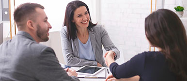 Drei Personen sitzen am Tisch, zwei schütteln sich die Hände