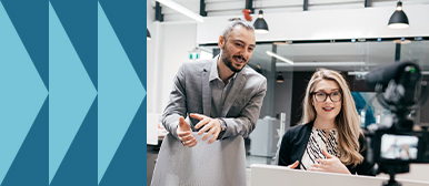 Eine Frau spricht vor einer Kamera, während ein Mann daneben etwas erklärt – Symbolbild für professionelle Content-Erstellung, zielgerichtete Verbreitung und mediengerechte Kommunikation.