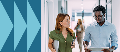 Eine Frau mit Laptop und ein Mann mit Tablet gehen durch ein modernes Büro und sprechen miteinander – Symbolbild für strategische Content-Planung, mobile Zusammenarbeit und zielorientierte Kommunikation.