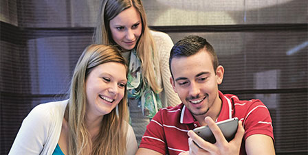 drei Studierende, die auf ein IPad schauen