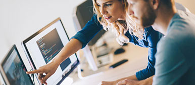 Frau und Mann vor einem Bildschirm, sie zeigt ihm etwas