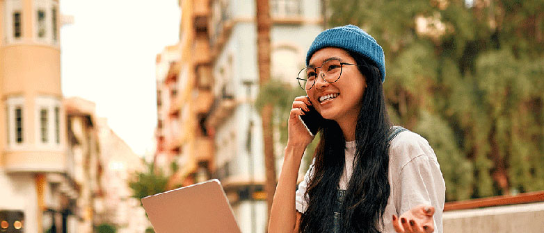 Junge Frau mit Laptop und Smartphone vor Stadtkulisse