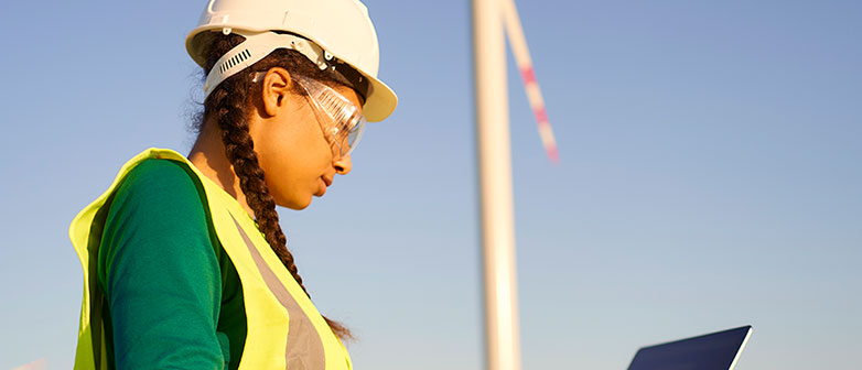 Frau mit Helm und Laptop vor einem Windrad