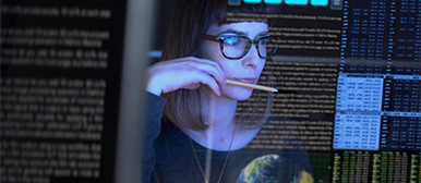 Blaues Bildschirmlicht reflektiert sich in Gesicht von Frau,  um sie herum sind Programmiercodes grafisch eingefügt