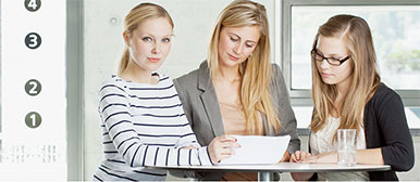 Drei blonde Studentinnen schauen sich gemeinsam an einem Hochtisch ein Dokument an