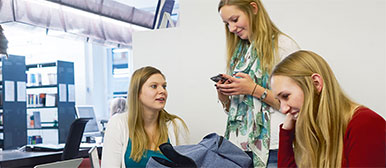 Drei blonde freudige Frauen am arbeiten in einer Büro-Umgebung, eine ist beschäftigt am Handy