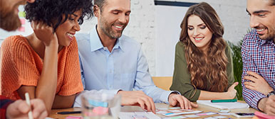 Mehrere Personen schauen auf verschiedene Karten, welche auf einem Tisch liegen.