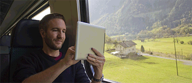 Junger Mann rast im Zug durch die Schweizer Landschaft und arbeitet remote.