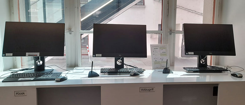 Drei Bildschirme auf einem langen Tisch