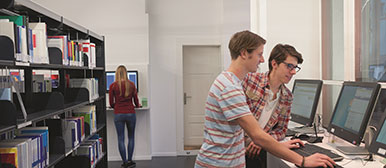 Drei Personen arbeiten stehend an zwei Bildschirmen